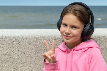 Cute Little girl in pink hoodie listening music at wireless headphones