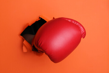 Man breaking through orange paper with boxing glove, closeup