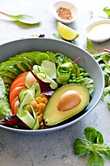 Healthy vegetarian food. Fresh vegetables cucumber, tomato, corn, green peas, avocado, lettuce in a bowl on a blue background. Healthy eating concept.
