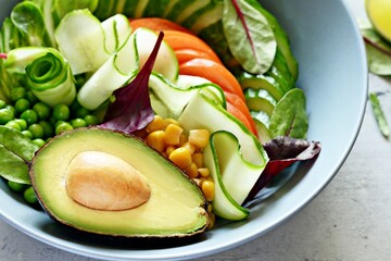 Healthy vegetarian food. Fresh vegetables cucumber, tomato, corn, green peas, avocado, lettuce in a bowl on a blue background. Healthy eating concept.