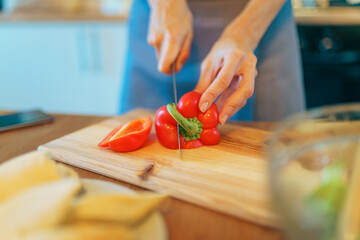Woman standing in kitchen slicing red pepper for salad. Prepare healthy meal
