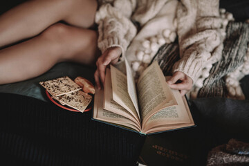 Cropped young woman in a cozy knitted sweater reading a book on the bed. Home aesthetics. Winter concept