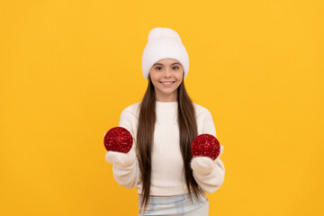 happy kid in winter hat and gloves hold decorative new year balls on yellow background, xmas