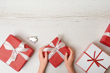 Child packs Christmas gifts on a white background, place for text. Red and white gift boxes on a...