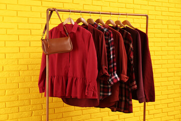 Rack with stylish clothes and bag near yellow brick wall