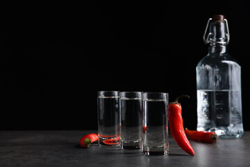 Red hot chili peppers and vodka on grey table against black background, space for text