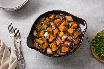 Baked lentils with pumpkin and onions in ceramic mold on a gray textured background, top view. Delicious homemade food