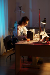 Busy tailor woman working late at night sit at table with sewing machine, fabric and paper patterns in studio creating new collection for small atelier opening. Tailoring entrepreneurship concept