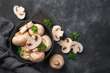 Fresh, raw champignons with parsley in a frying pan on a black background.