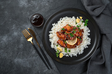 Chicken in sweet and sour sauce and rice on a black background.