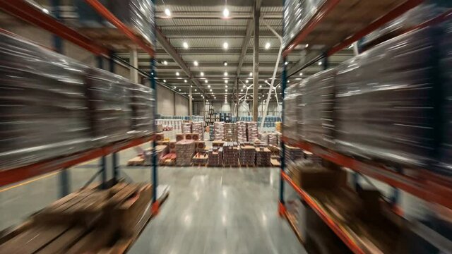 Time-lapse view inside warehouse. FPV flight between rows of shelves with delivery goods. Plenty of cardboard boxes on industrial racks. Logistic center.