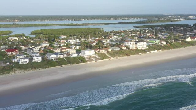 Aerial pan of Florida east coast barrier island beachfront community Wilbur By The Sea, showing beach, ocean surf, residential houses with sea walls, and the Atlantic Intracoastal Waterway.