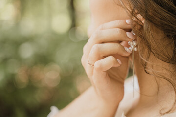 the bride straightens her earring on the background of greenery close-up
