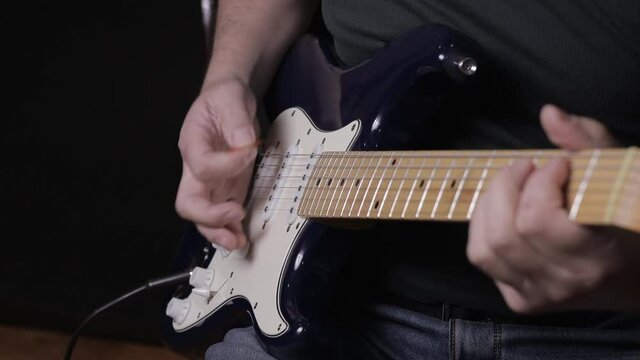 A male musician plays a melody on a blue six-string guitar.