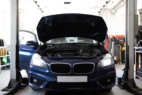 Photo of a blue passenger car at the service station being repaired with an open hood