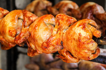 Close-up of roasted whole chicken with tasty golden skin on a rotisserie in a row in a street food booth