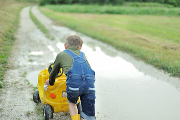 A little boy is playing with  toy cars in a huge puddle.  © Jacek