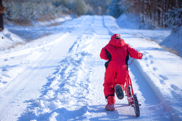 A child in a red winter jacket is riding a scooter in the snow.