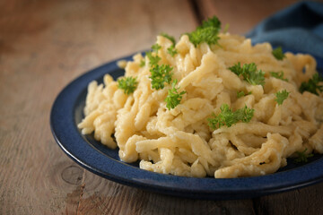 Homemade spaetzle, German egg noodles with cheese served with parsley garnish on a blue plate and a...