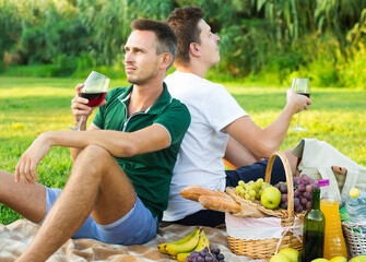 adult man with a friend enjoying picnic on summer day, sitting back to back
