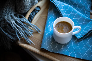 Black coffee in white mug with elegant blue napkin on wooden tray