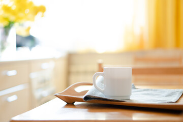 White coffee mug with napkin on table in real kitchen interior with bright natural sunlight