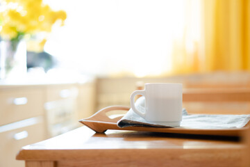 White coffee mug with napkin on table in real kitchen interior with bright natural sunlight