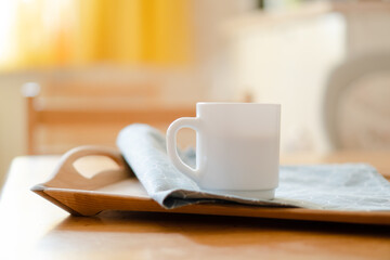 Fototapeta na wymiar White coffee mug with napkin on table in real kitchen interior with bright natural sunlight