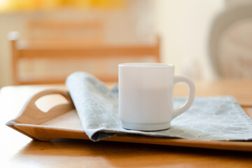 White coffee mug with napkin on table in real kitchen interior with bright natural sunlight