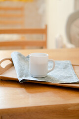 White coffee mug with napkin on table in real kitchen interior with bright natural sunlight