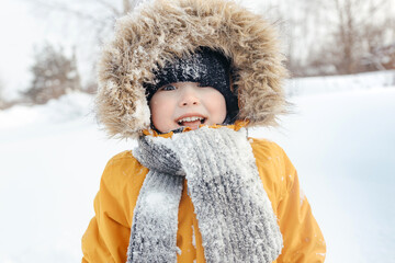 smiling child in a fur hood in a knitted scarf and an orange winter jacket. outdoors. fashionable child. children. close-up. winter