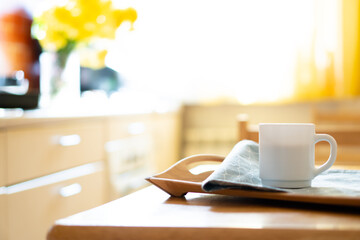 White coffee mug with napkin on table in real kitchen interior with bright natural sunlight