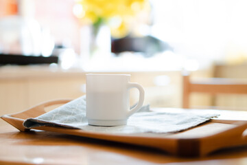 White coffee mug with napkin on table in real kitchen interior with bright natural sunlight