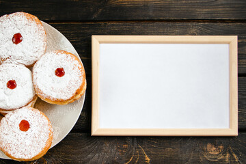 Happy Hanukkah. Empty frame for congratulations text and traditional dessert Sufganiyot on dark wooden background. Celebrating Jewish holiday.