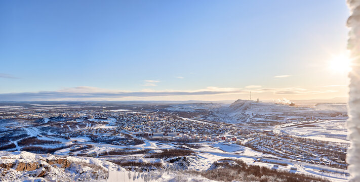 View of Kiruna city and the iron ore mine on the mountain Kiirunavaara seen from the snowy frozen mountain peak Luossavaara with low standing sun.