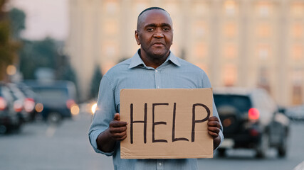 Sad stressed frustrated elderly african american poor man retirement age, lost tourist, holding cardboard banner with inscription need help asks for money crisis health problems during covid pandemic