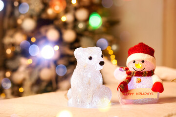 Glowing christmas bear and snowman on bed with christmas tree and garland lights on background