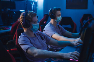 Professional players in masks training or playing online video game on PC late at night