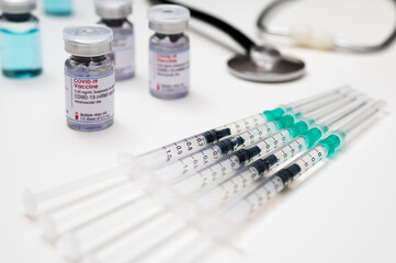 Coronavirus vaccination against SARS-CoV-2. Medical syringes, each with a dose of COVID-19 vaccine; in the background: several glass vials and a stethoscope