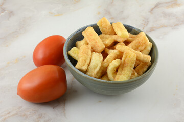 Spicy tomato flavored corn snack in bowl with fresh raw tomatoes