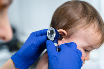 Red-haired female doctor examines little child for less than a year in a modern clinic....