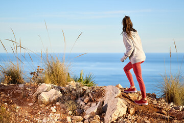 athletic woman with long hair and red leggings climbing uphill in the mountains