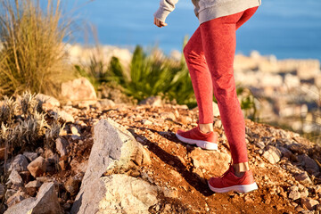 athletic woman with long hair and red leggings climbing uphill in the mountains