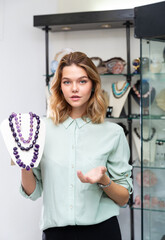 Fototapeta na wymiar Portrait of happy young woman demonstrating natural amethyst stone necklace in shop