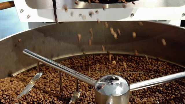 Coffee roaster machine at coffee roasting process. Mixing coffee beans. Roasted spinning cooler professional machines and fresh brown coffee beans movement close-up dark photo at factory
