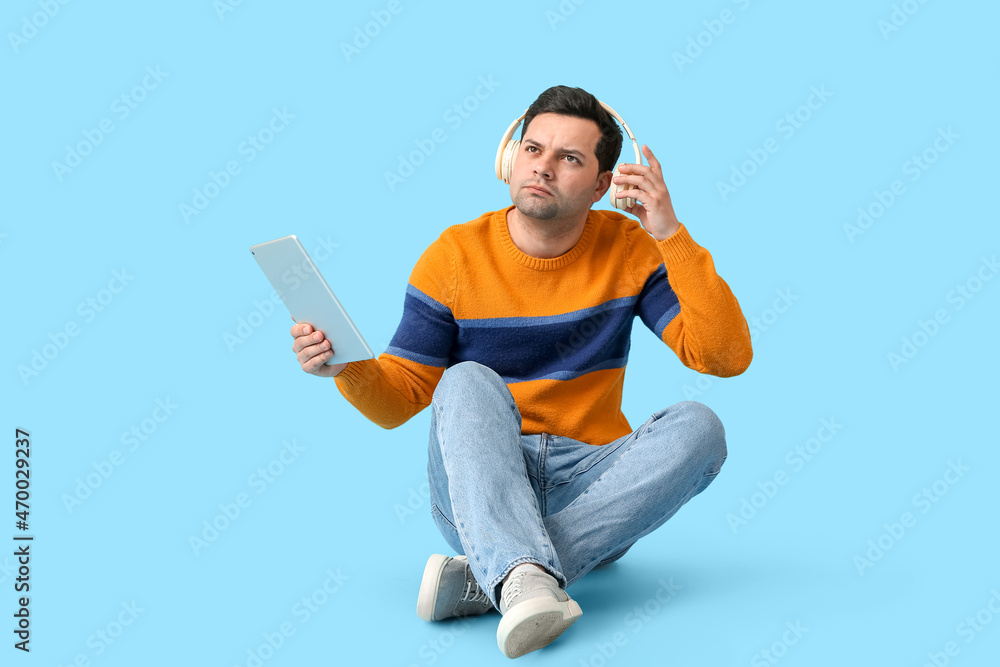 Wall mural Young man with tablet computer and headphones on color background