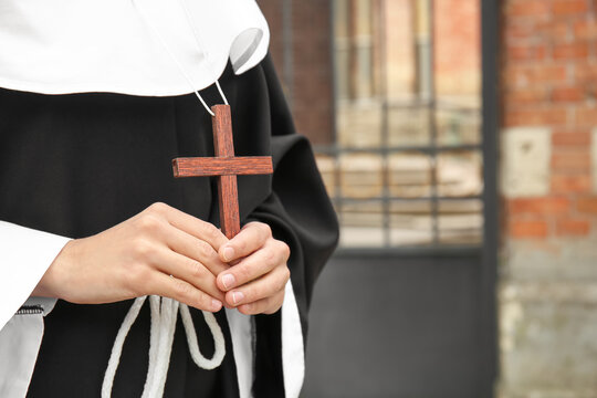 Young nun with wooden cross in hands near church