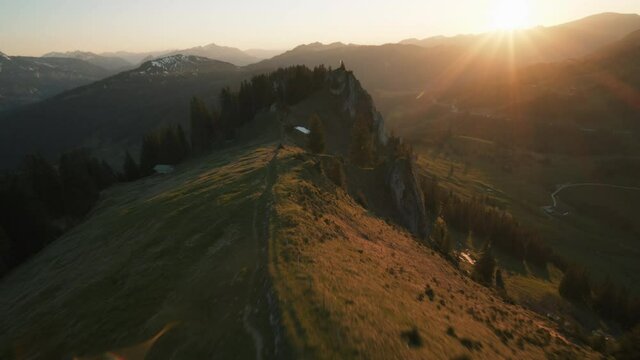 Fpv drone shot over a mountain and diving down through trees to a valley, during sunset