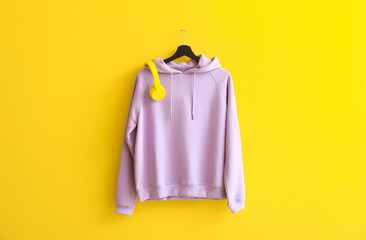 Modern hoodie with headphones hanging on color wall