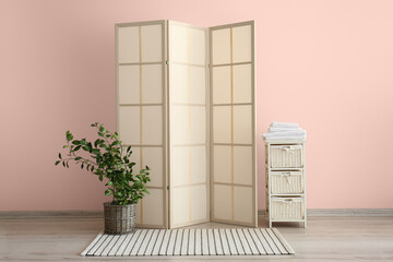 Stylish folding screen and chest of drawers with towels near wall in room